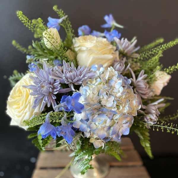 Bouquet of cream roses, blue flowers, and lavender blooms in a glass vase