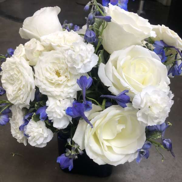 White roses and carnations with blue accents in a black vase