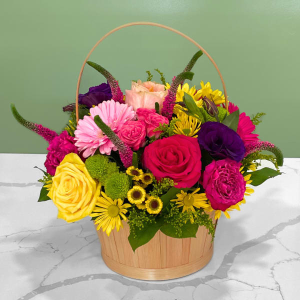 Mixed bouquet in a wooden basket with pink, yellow, and purple flowers