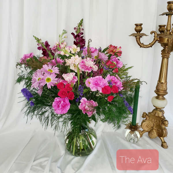 Pink and purple mixed bouquet in a glass vase beside a gold candlestick