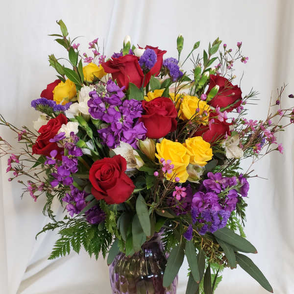 Mixed bouquet of red, yellow, and purple flowers in a purple glass vase