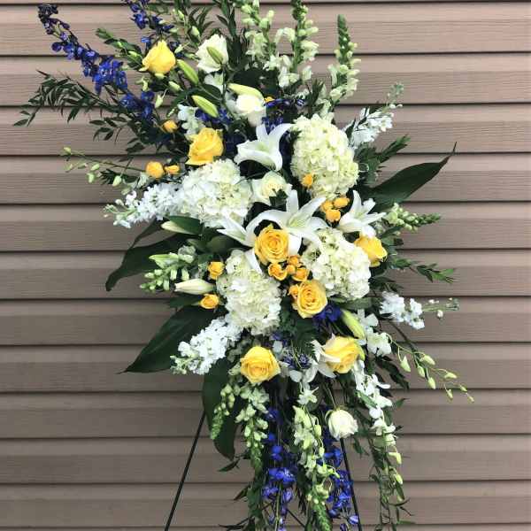 Standing floral spray with white lilies, yellow roses, and blue flowers
