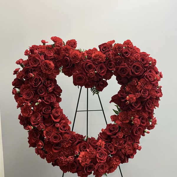 Heart-shaped red rose and carnation floral wreath on a stand