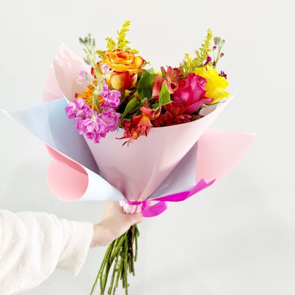 Handheld bouquet of multicolored roses and mixed blooms in pastel wrap