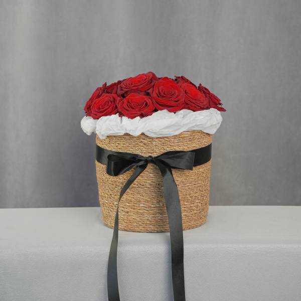 Red roses arranged in a woven hatbox with a black ribbon
