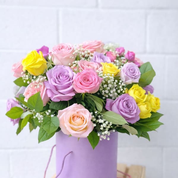 Pastel pink, lavender, and yellow roses with baby’s breath in a lavender hatbox container