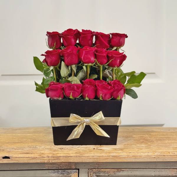 Red roses arranged in a black box with a gold ribbon
