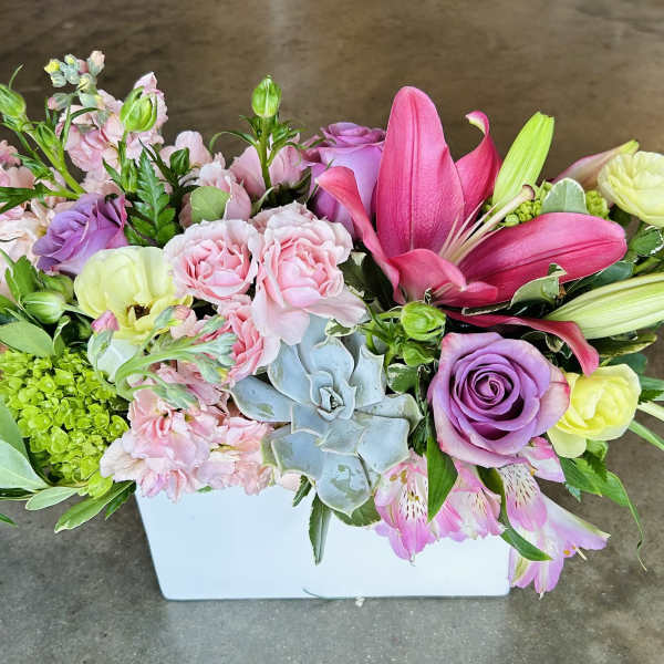 Mixed pink and purple floral arrangement in a white rectangular vase