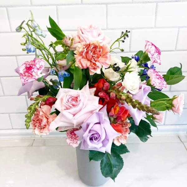 Mixed bouquet of pastel roses, carnations, and blue flowers in a gray vase
