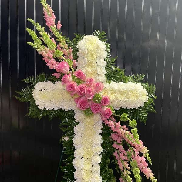 White floral cross with pink roses and snapdragons on a dark background