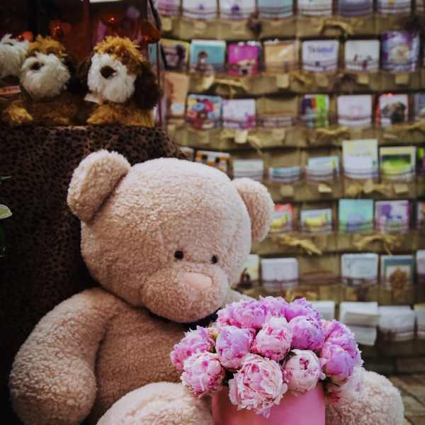 Pink teddy bear with a box of pink flowers and two smaller plush dogs behind it