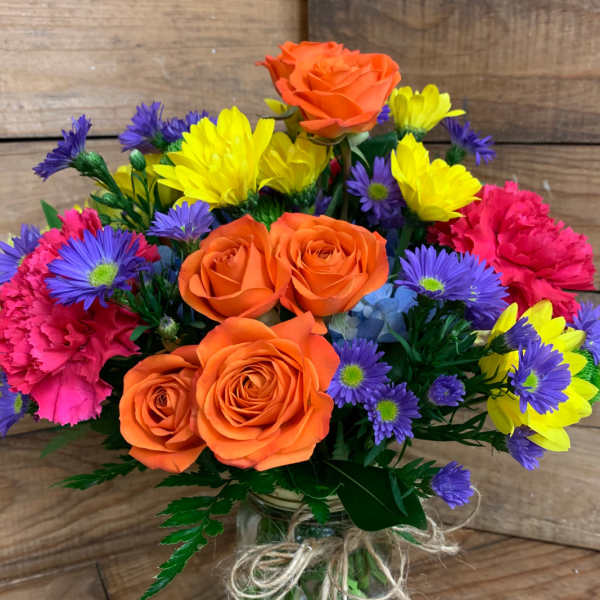 Bouquet of orange roses and colorful daisies in a glass vase