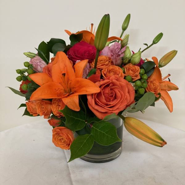 Orange lilies and roses arranged in a glass vase