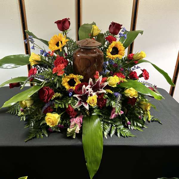 Large floral arrangement with roses, sunflowers, lilies, and a brown urn centerpiece