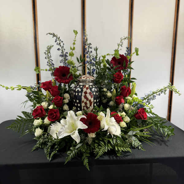 Red roses, white lilies, and gerbera daisies arranged around a patriotic urn