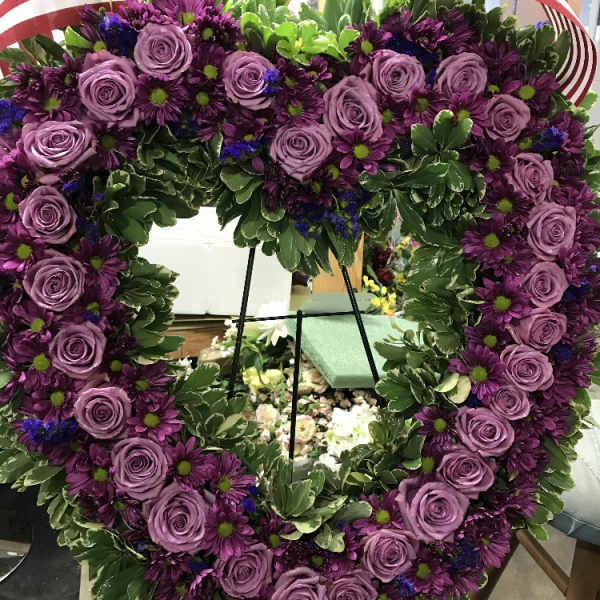 Heart-shaped floral wreath with purple roses and daisies on an easel