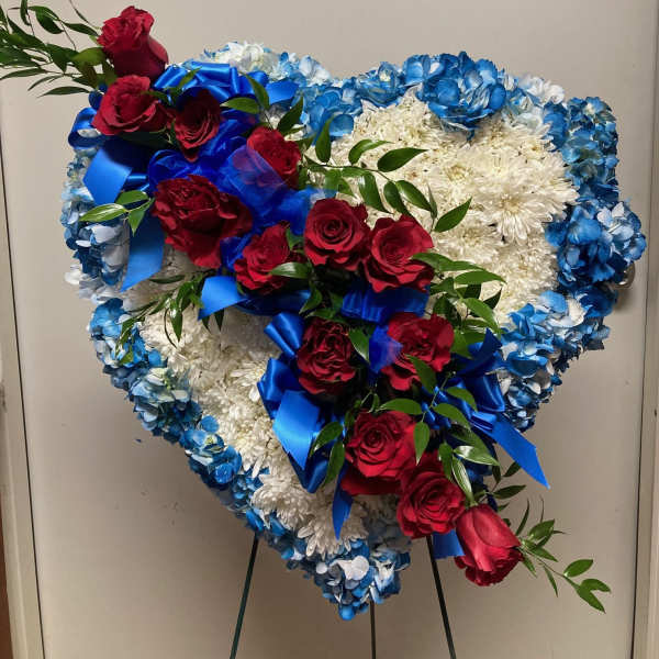 Heart-shaped floral tribute with red roses, white blooms, and blue accents