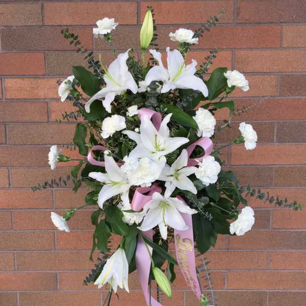 Standing white lily and carnation spray with pink ribbon on an easel