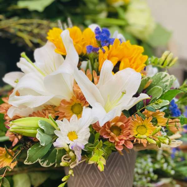 Bouquet of white lilies, yellow and peach daisies in a gray vase