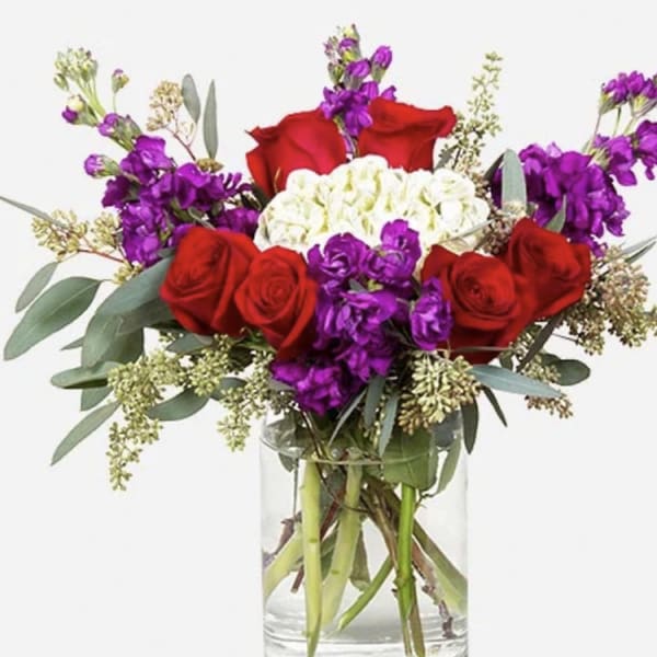 Bouquet of red roses, purple flowers, and white blooms in a glass vase