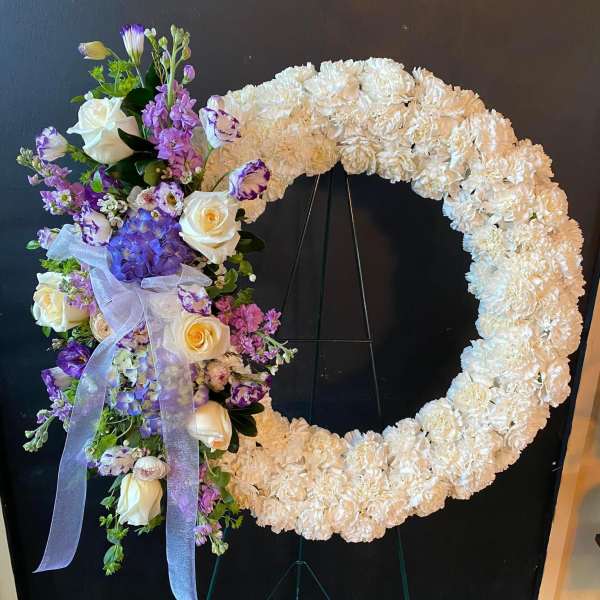 Large floral wreath on an easel with white and purple flowers and a lavender ribbon