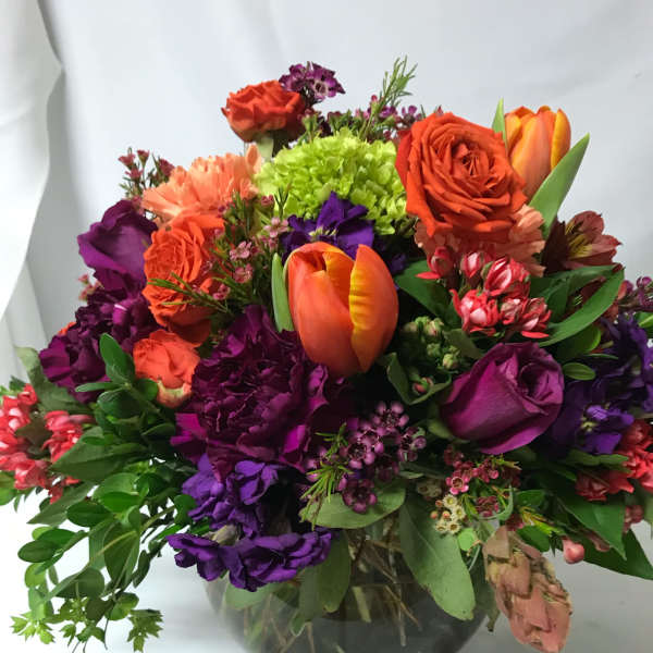 Mixed bouquet of orange, purple, and lime flowers in a glass vase