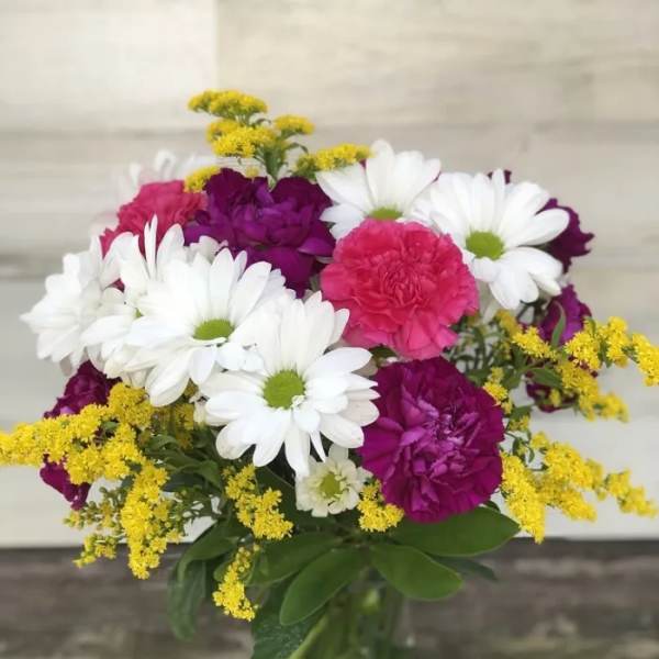Bouquet of white daisies, pink carnations, and yellow filler in a glass vase
