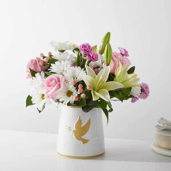 Pink and white flowers arranged in a white vase with a gold dove design