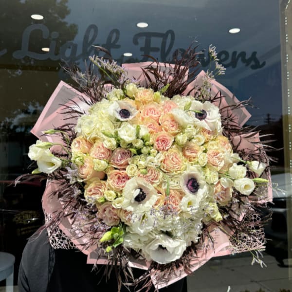 Large bouquet of pale roses and white flowers wrapped in pink paper