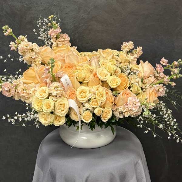 Peach and pale yellow roses arranged in a white bowl vase