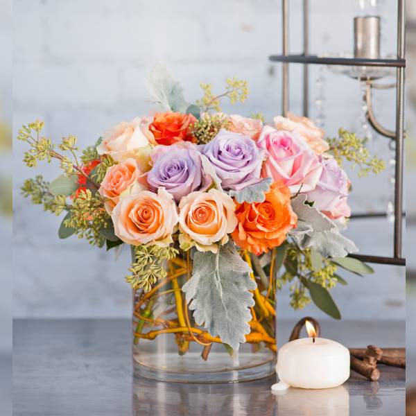 Mixed roses in a clear glass vase beside a lit candle