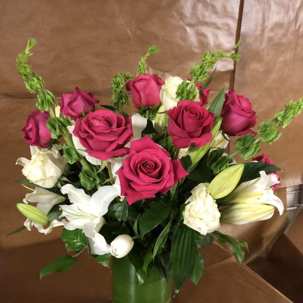 Pink and white roses with lilies in a green glass vase
