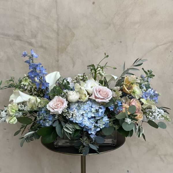 Pastel floral arrangement with blue hydrangeas, pink roses, and white calla lilies in a low vase