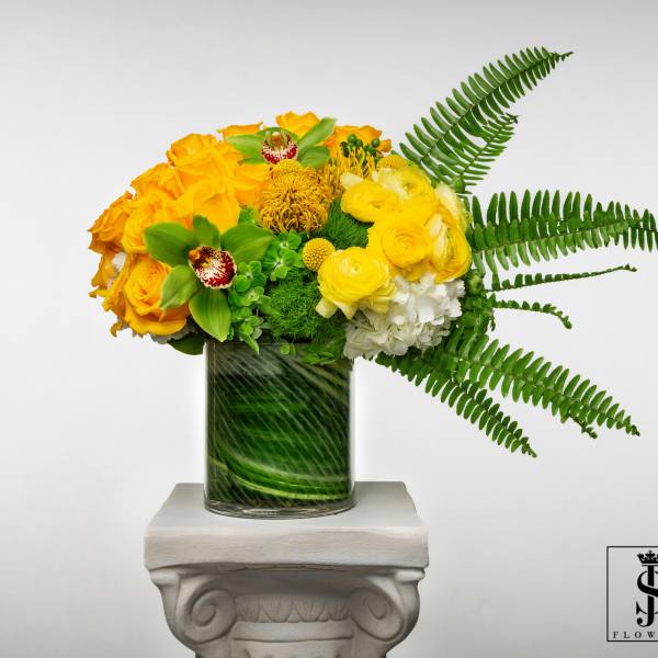 Yellow floral arrangement in a glass vase with fern fronds