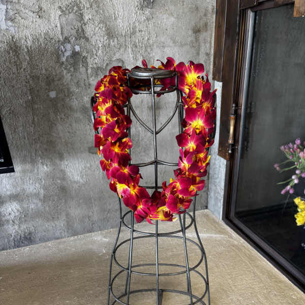 Red and yellow orchid lei draped over a black metal stand