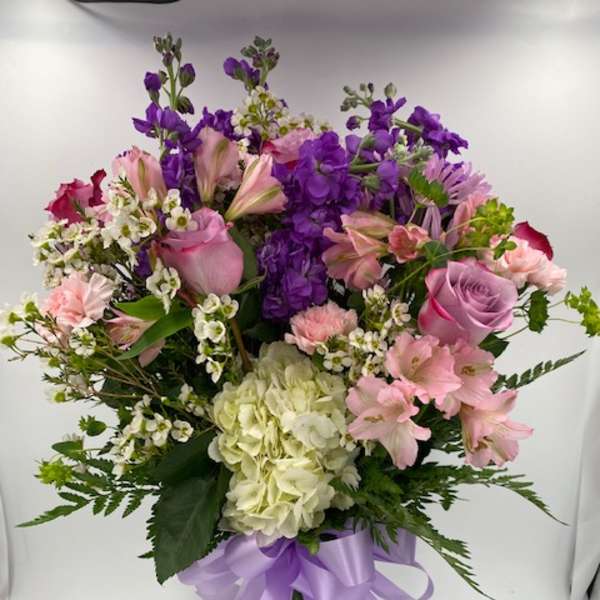 Mixed pink and purple bouquet in a clear glass vase with a lavender ribbon