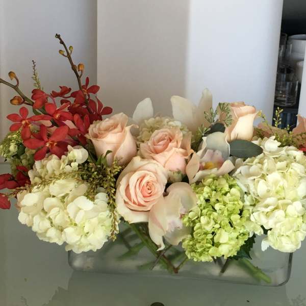 Arrangement of peach roses and white hydrangeas with red orchids in a glass vase