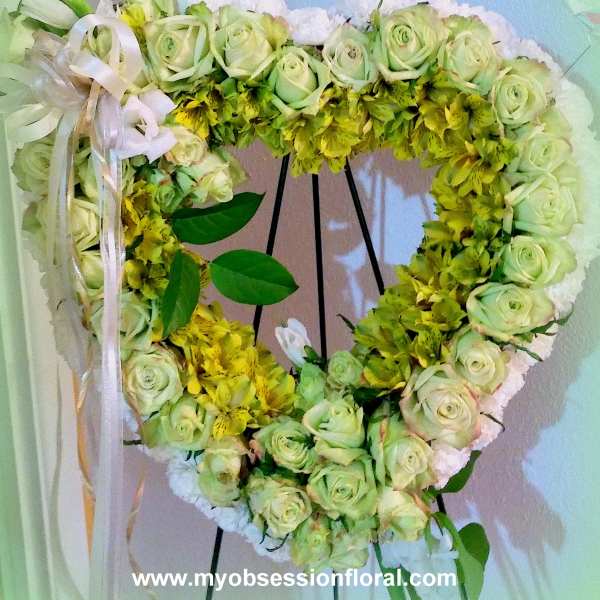 Heart-shaped floral wreath with pale green roses and yellow flowers on a stand