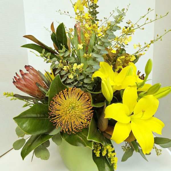 Yellow lilies and a protea in a vase with mixed greenery