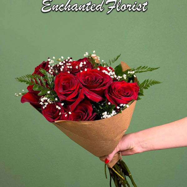Handheld bouquet of red roses wrapped in brown paper against a green background