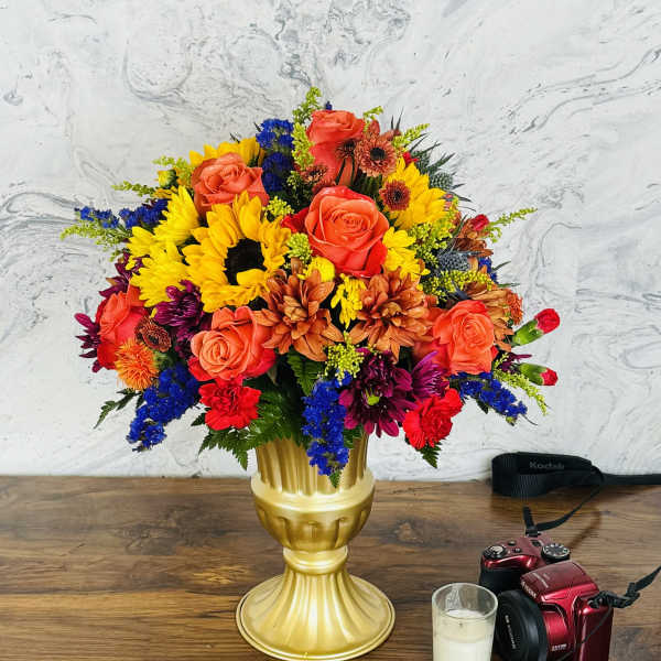 Colorful bouquet of roses, sunflowers, and mixed blooms in a gold vase