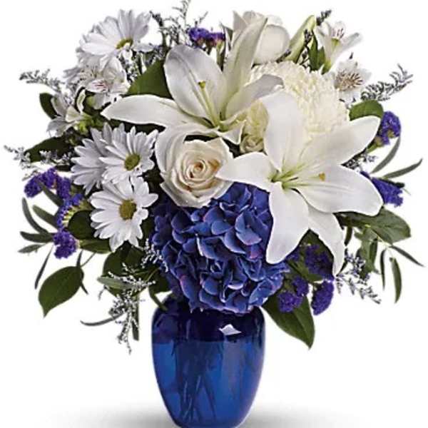 White lilies and daisies with blue hydrangea in a cobalt vase