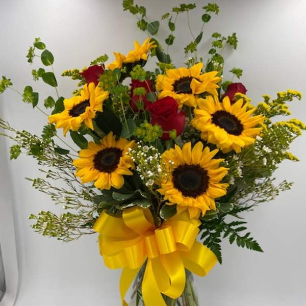 Bouquet of sunflowers and red roses in a glass vase with a yellow ribbon