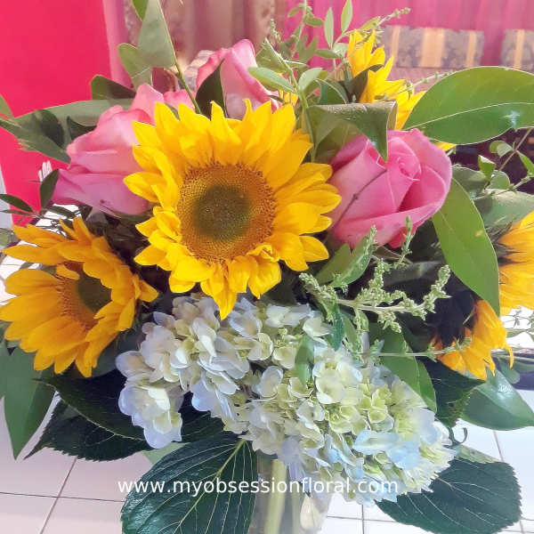 Bouquet of sunflowers, pink roses, and pale hydrangeas in a glass vase