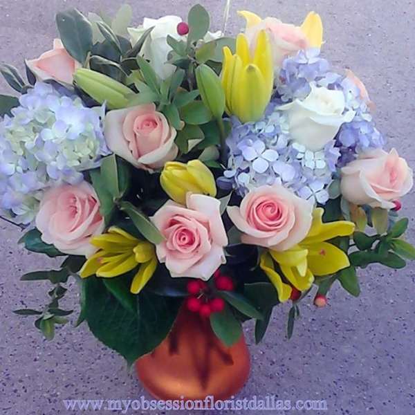 Bouquet of pink roses, yellow lilies, and blue hydrangeas in a vase