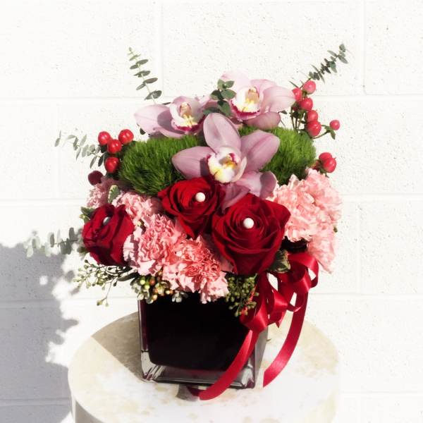 Pink orchids and red roses in a black vase with a red ribbon