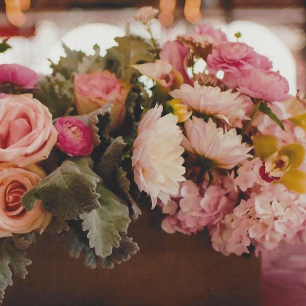 Pink and peach floral centerpiece with roses and daisies in a low container