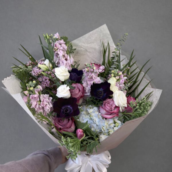 Hand-tied bouquet of pink, white, and dark purple flowers wrapped in paper