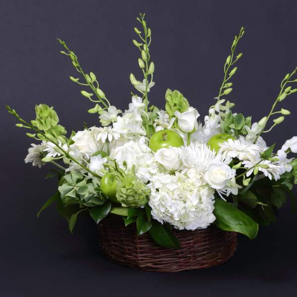 White floral arrangement in a wicker basket with green apples