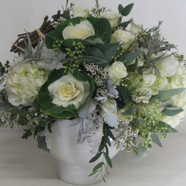 White floral arrangement in a white vase with trailing greenery